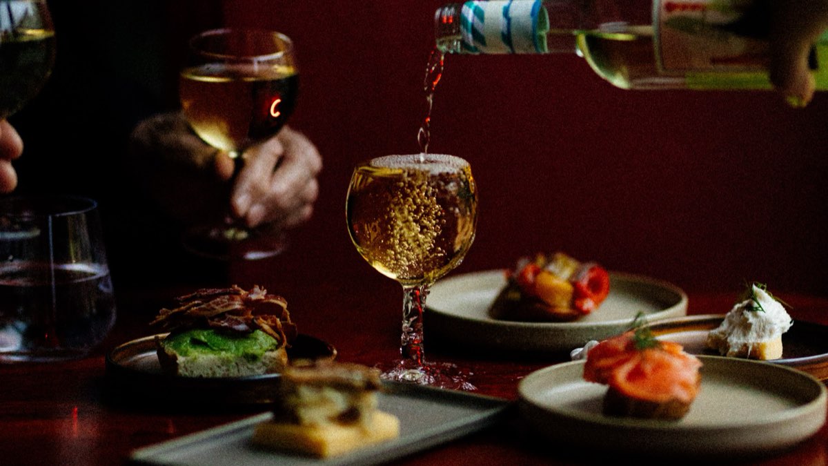 Wino nalewane do kieliszka nad talerzami cicchetti, w tle czerwony trawertyn