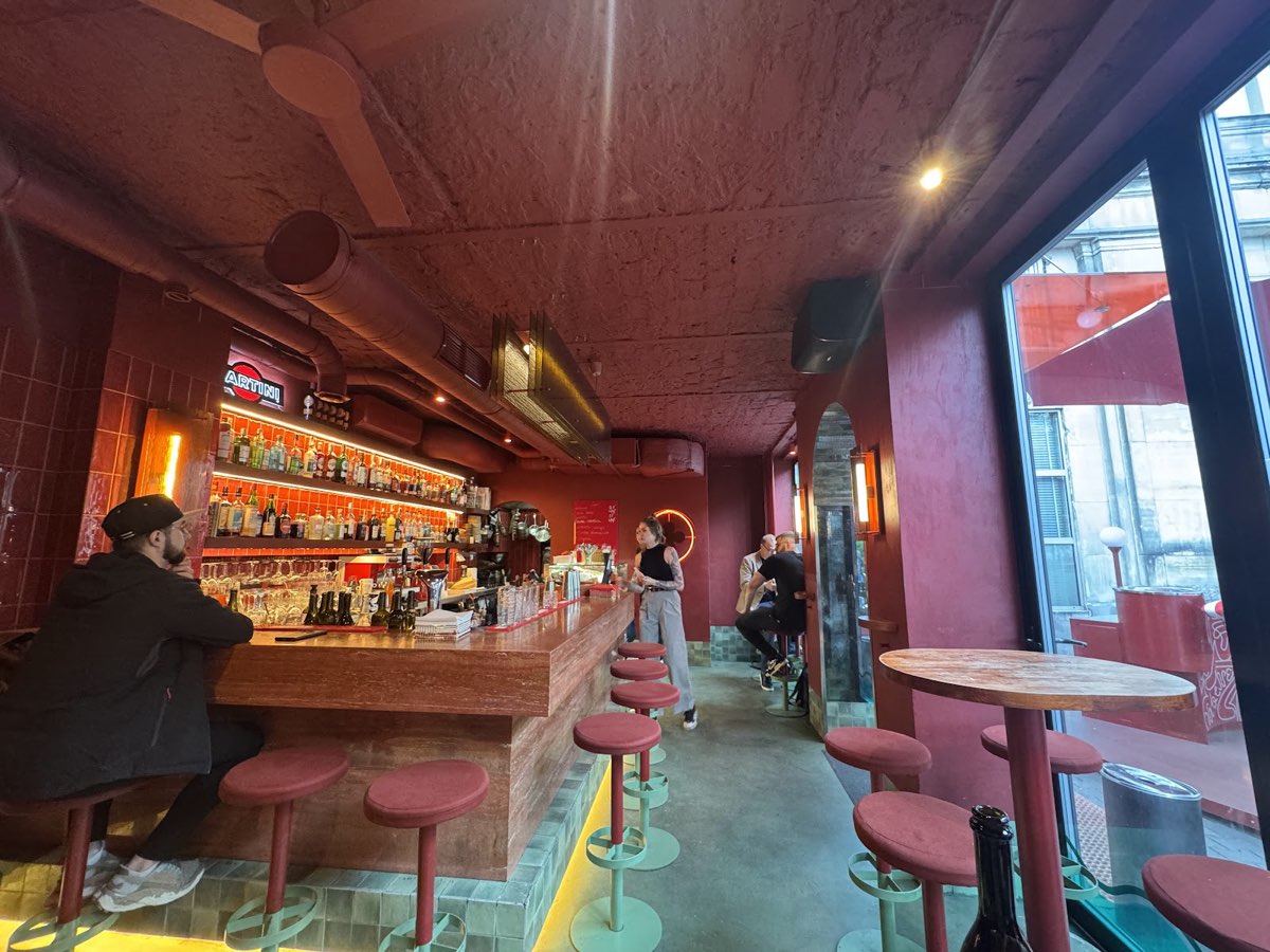 Bar z czerwonego trawertynu, czerwone stołki i lazurowo-zielona podłoga Aqua Alta we wnętrzu Va Bene Cicchetti