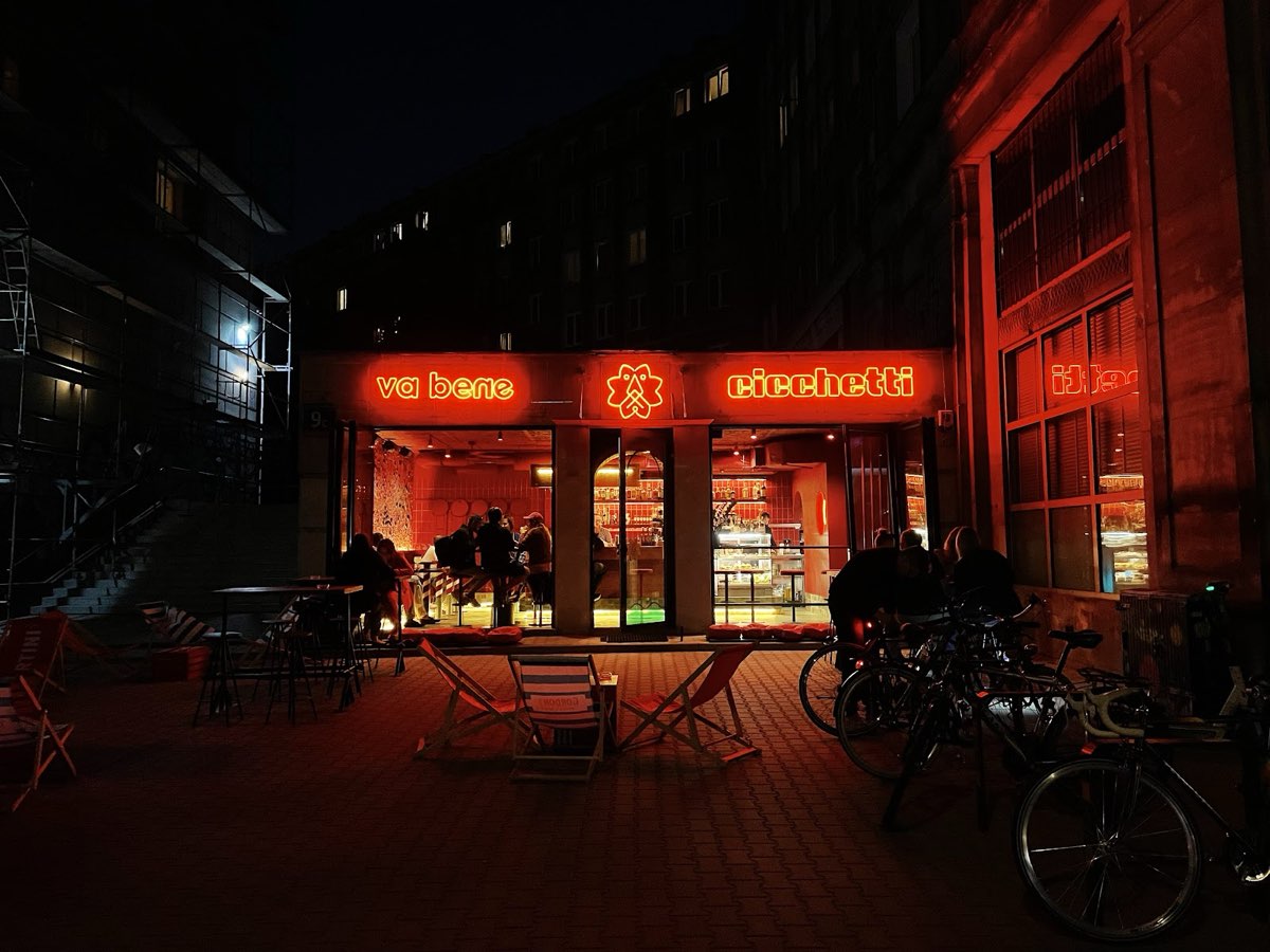 Witryna lokalu nocą, neon va bene cicchetti i skrzydlaty lew, leżaki i goście na zewnątrz
