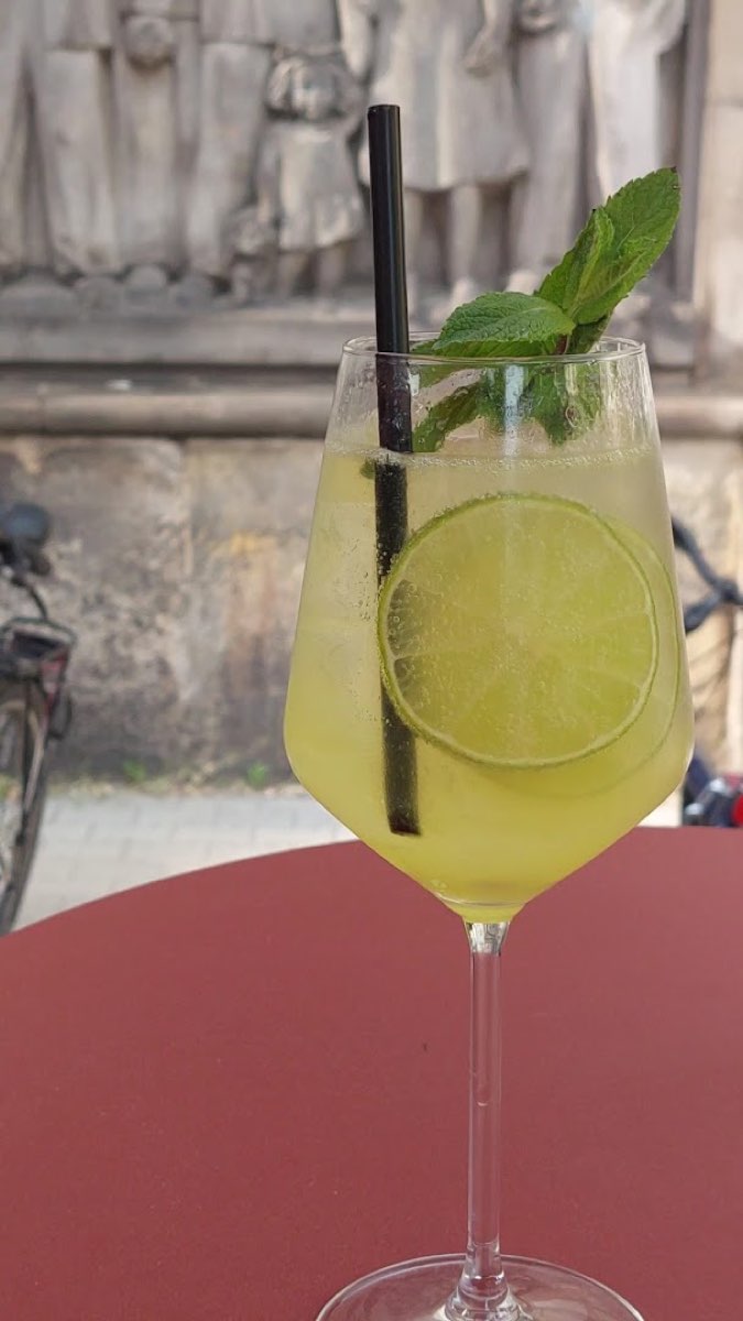 Ziołowy, jasny koktajl typu spritz w wysokim kieliszku, na zewnątrz lokalu