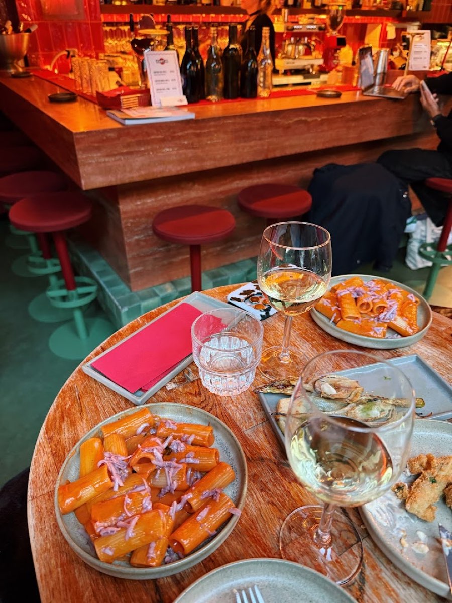 Małe talerze cicchetti, rigatoni i ostrygi na stoliku w kształcie weneckiego pala cumowniczego, na lazurowo-zielonej podłodze Aqua Alta